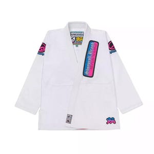 May include: White Jiu-Jitsu Gi with pink and blue accents. The Gi features the text "Shoyoroll Brand" on the sleeve and the text "Shoyoroll Kimonos" on the collar.
