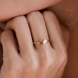 May include: A gold ring with two small, pear-shaped stones set in the band.