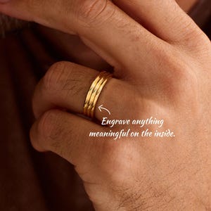May include: A gold-toned ring with a triple-band design featuring three parallel ridges. The ring is shown with a white arrow pointing to the band and the text: Engrave anything meaningful on the inside.