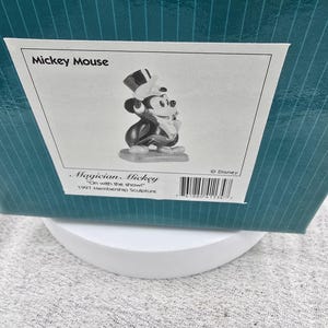 May include: A black and white Mickey Mouse figurine in a magician's outfit, including a top hat and tuxedo. The figurine is part of the 1997 Membership Sculpture collection. The box reads "Mickey Mouse" and "Magician Mickey".