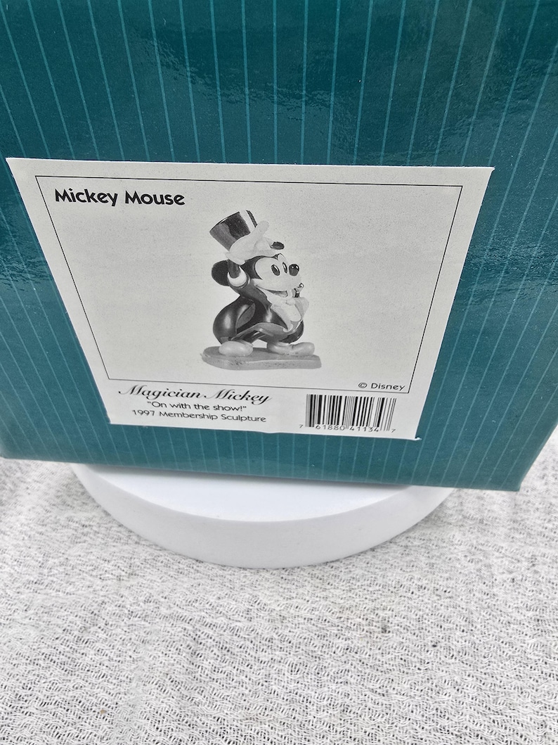 May include: A black and white Mickey Mouse figurine in a magician's outfit, including a top hat and tuxedo. The figurine is part of the 1997 Membership Sculpture collection. The box reads "Mickey Mouse" and "Magician Mickey".