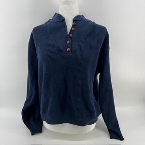 May include: A navy blue long-sleeve sweater featuring a ribbed knit texture and a mock neck collar. The front placket includes five small, round, reddish-brown buttons arranged vertically, extending from the collar down to the upper chest area.