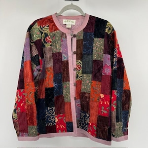 May include: A long-sleeved jacket featuring a patchwork design of various corduroy and floral fabric squares in shades of red, purple, black, and orange. The jacket has a round neckline, a light pink trim, and five dark brown buttons down the front.