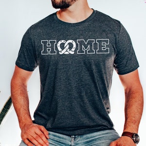 Op de afbeelding: Een donkergrijs T-shirt met een witte afbeelding van het woord "HOME" met een pretzel in plaats van de "O".