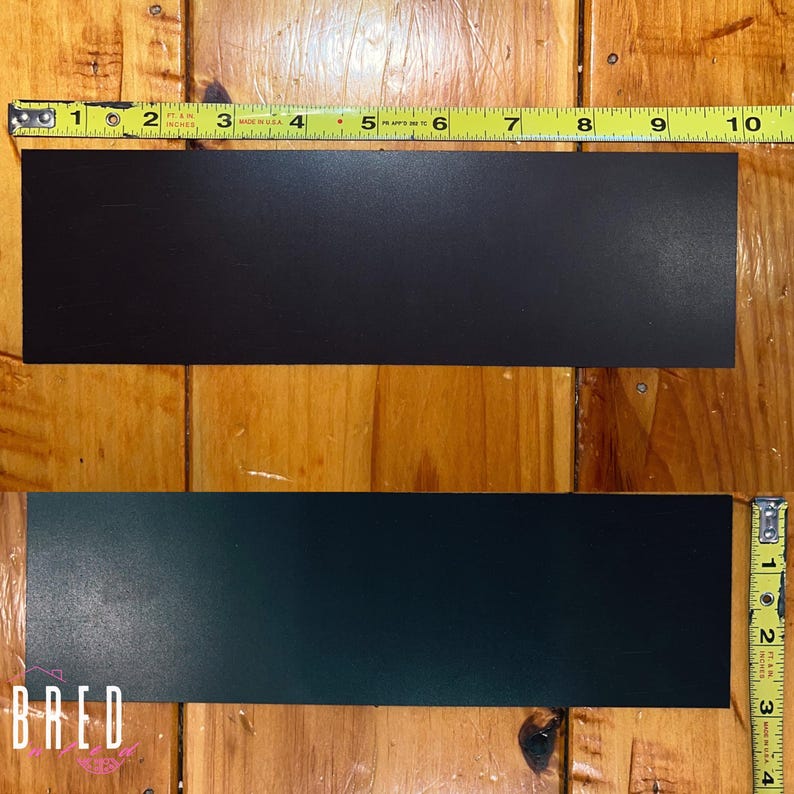 The black back side of a 10 x 3 inch rectangular car magnet laying flat on a wooden floor with tape measures showing the 10 inch length and the 3 inch height dimensions.