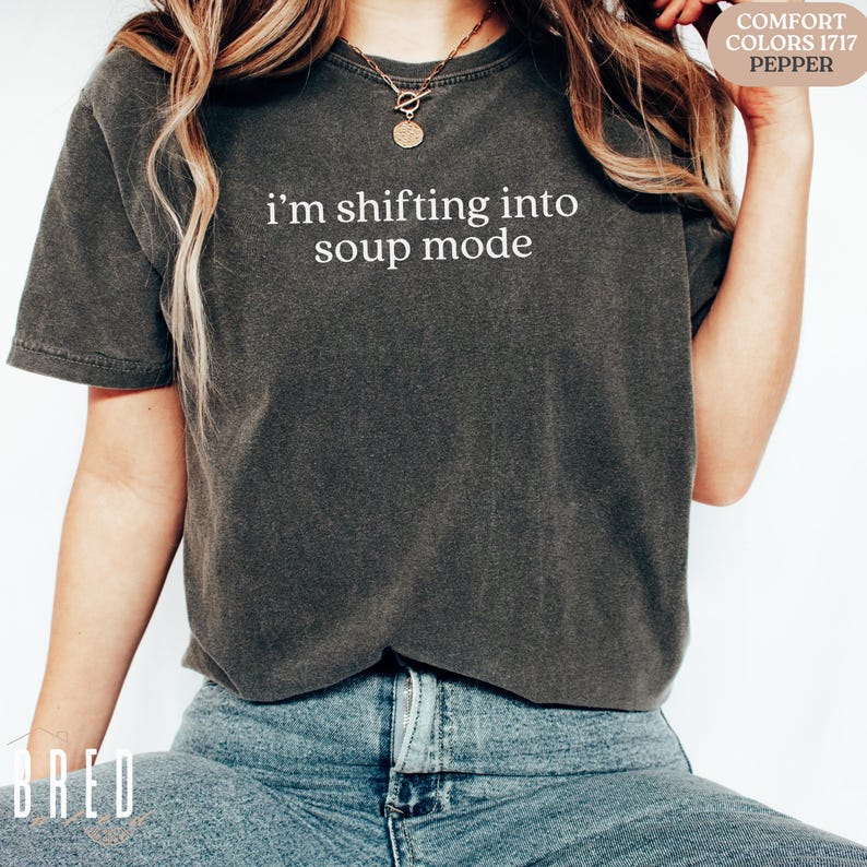 Woman wearing pepper Comfort Colors shirt that says, “i'm shifting into soup mode,” relaxed fit. Funny Seinfeld shirt for fans of soup and 90s sitcom lovers.
