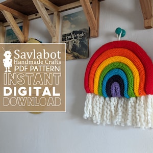 Op de afbeelding: Een kleurrijke regenboog gehaakte wanddecoratie met een witte franje. De regenboog is gemaakt van rood, oranje, geel, groen, blauw, indigo en violet garen. De tekst "Savlabot Handmade Crafts PDF Pattern Instant Digital Download" staat op een bruine rechthoek.