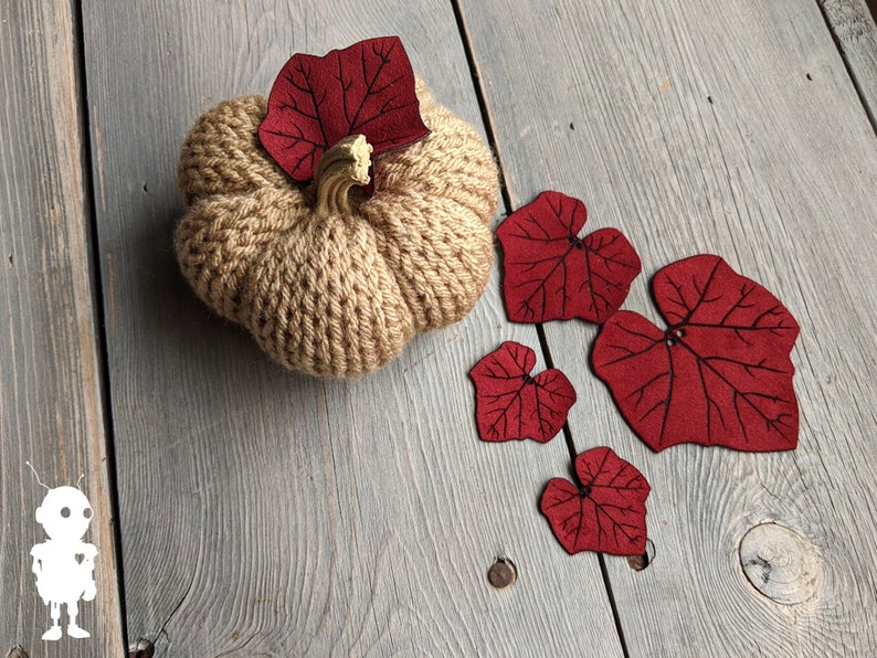 May include: A knitted brown pumpkin with a stem and five red felt leaves.