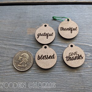 May include: Four round wooden charms with the words "grateful", "thankful", "blessed", and "give thanks" engraved on them. The charms are about the size of a US quarter.