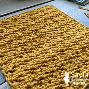 May include: A close-up of a crocheted square made with a mustard yellow yarn. The square is made with a textured stitch pattern. The image includes the text "Savlabot Handmade Crafts PDF Pattern".