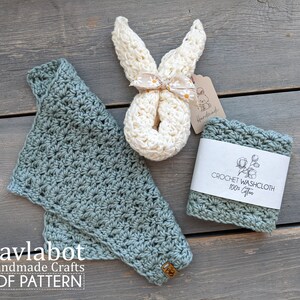 May include: Two crocheted washcloths, one in a light green color and one in a cream color. The cream washcloth is shaped like a bunny and is tied with a ribbon. The washcloths are on a wooden surface with a tag that says "Crochet Washcloth 100% Cotton".