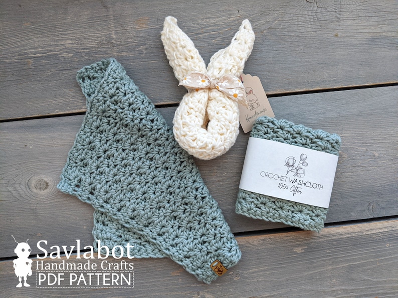 May include: Two crocheted washcloths, one in a light green color and one in a cream color. The cream washcloth is shaped like a bunny and is tied with a ribbon. The washcloths are on a wooden surface with a tag that says "Crochet Washcloth 100% Cotton".