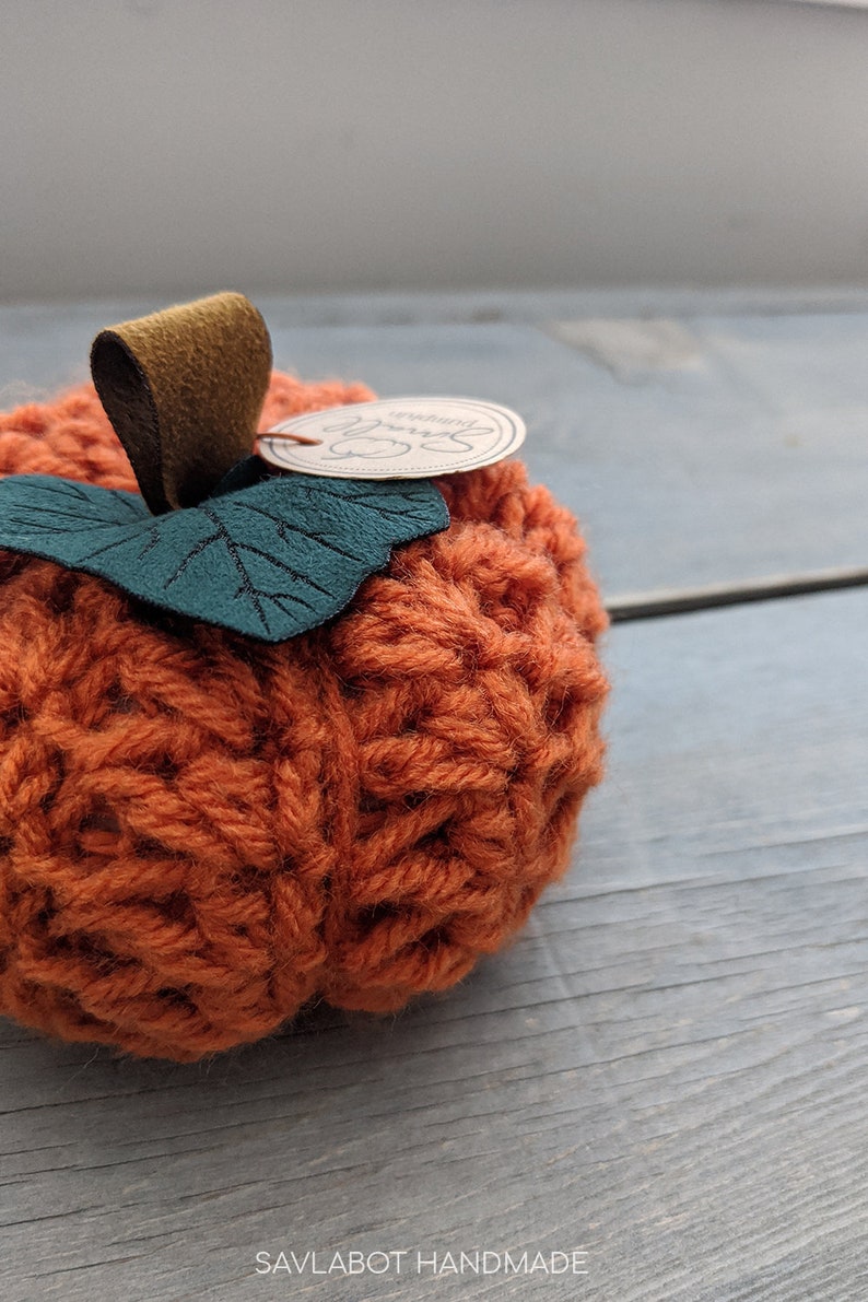 May include: A crocheted orange pumpkin with a green felt leaf and a brown leather stem. The pumpkin has a small tag attached to it that says "Savlabot Handmade".