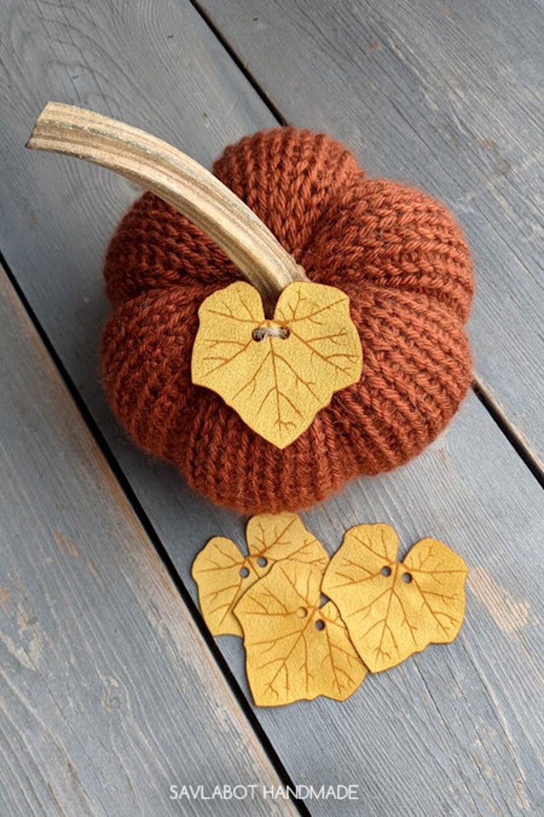 May include: A knitted pumpkin with a brown stem and a felt leaf accent. The pumpkin is surrounded by four additional felt leaves.