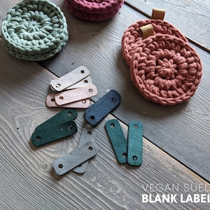 Peut inclure: Un ensemble de dessous de verre en crochet de couleur verte, rose et grise, avec un ensemble d'étiquettes en daim végétalien vierges en vert, gris, rose et bleu. Le texte "VEGAN SUEDE BLANK LABELS" est visible sur l'image.