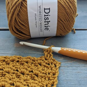 May include: A ball of mustard yellow worsted weight yarn labeled "Dachie" with 190 yards/100 grams. A crochet hook is shown with a crocheted square made with the yarn.