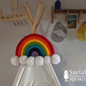 May include: A colourful rainbow crocheted wall hanging with white pom pom clouds. The rainbow is made of red, orange, yellow, green, blue, purple, and lavender yarn. The rainbow is hanging on a white teepee tent.