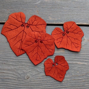 May include: Four felt leaf shapes in shades of orange and red with stitched details. The leaves are arranged on a gray wooden surface.