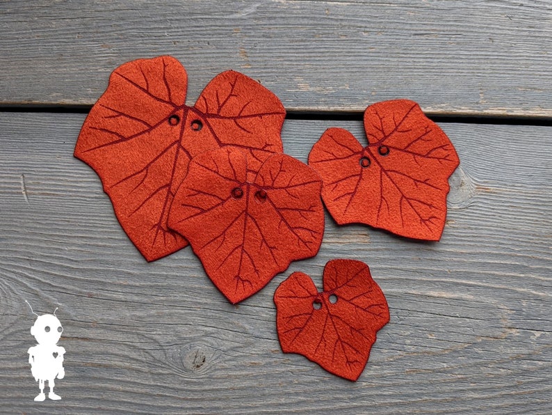 May include: Four felt leaf shapes in shades of orange and red with stitched details. The leaves are arranged on a gray wooden surface.