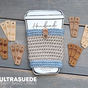 May include: A beige and light blue crocheted cup cozy wrapped around a paper coffee cup cutout labeled Handmade. The cozy features a small brown leather tag with a coffee cup icon. Several rectangular tan leather labels with coffee bean icons.