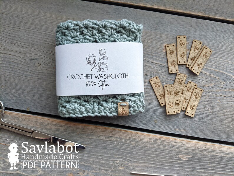 May include: A crocheted washcloth made of 100% cotton, with a label that reads "Crochet Washcloth 100% Cotton". The washcloth is light blue and has a floral design. There are also several small wooden tags with a floral design.