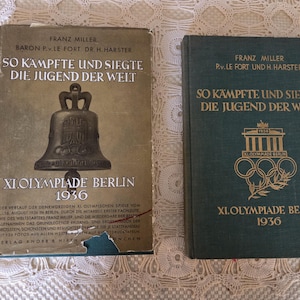May include: Two vintage books with German text. The book on the left has a bell illustration and the title "So Kämpfte und Siegte Die Jugend Der Welt" and "XI. Olympiade Berlin 1936". The book on the right has the same title and Olympic rings.