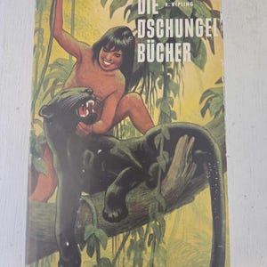 May include: Vintage book cover featuring a smiling person and a black panther on a tree branch, with jungle foliage in the background. The title "DIE DSCHUNGEL BÜCHER" is displayed in large, bold letters.