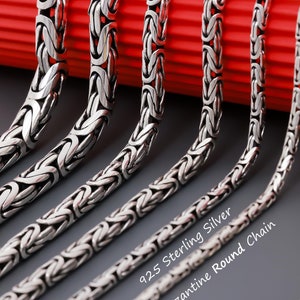 May include: Five silver chains of varying lengths, all featuring a Byzantine round chain design. The chains are arranged on a red surface and the text "925 Sterling Silver Byzantine Round Chain" is visible at the bottom of the image.
