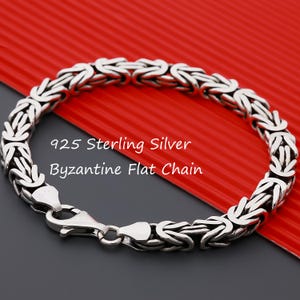 Puede incluir: Una pulsera de cadena plana bizantina de plata de ley 925 con un intrincado patrón de eslabones entrelazados y un cierre de mosquetón seguro. El texto 925 Sterling Silver Byzantine Flat Chain es visible en el centro de la imagen.
