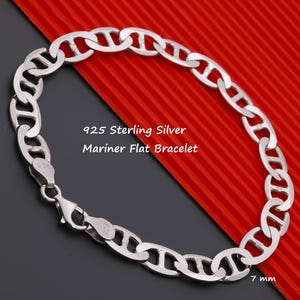 May include: A 925 sterling silver mariner flat bracelet featuring interlocking oval links with a central bar. The bracelet includes a lobster claw clasp and is marked with 925. The text 925 Sterling Silver Mariner Flat Bracelet and 7 mm is visible.