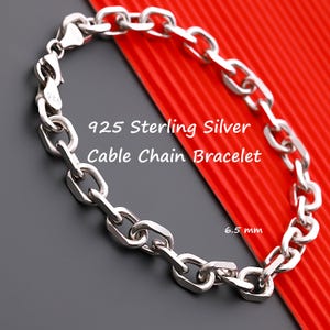 Puede incluir: Una pulsera de cadena de cable de plata de ley 925 con acabado pulido. La pulsera presenta eslabones ovalados entrelazados y un cierre de mosquetón. El texto 925 Sterling Silver Cable Chain Bracelet y 6,5 mm es claramente visible.