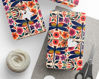 Peut inclure: Des cadeaux emballés avec un motif floral et libellule. Le papier d'emballage présente un fond crème avec des fleurs colorées et des libellules bleues. Chaque paquet est noué avec de la ficelle et une étiquette blanche. Une pelote de ficelle, des ciseaux et des étiquettes vierges sont également visibles.