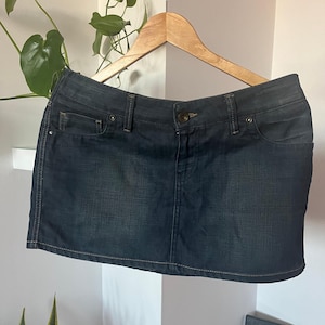 Op de afbeelding: Een donkerblauwe denim minirok met een klassiek vijf-zakken ontwerp. De rok hangt aan een houten hanger.