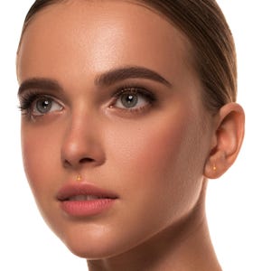 May include: Close-up of a person's face featuring a gold star-shaped lip piercing and a gold star stud earring. The skin is smooth and the background is white. The earrings and piercing are small and delicate.