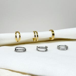 Könnte beinhalten: Fünf Ohrringe in Gold- und Silbertönen. Die Ohrringe haben Doppel- und Einzelreifen-Designs. Die Ohrringe werden auf einer weißen Oberfläche präsentiert.