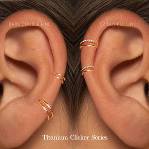May include: Close-up of two ears, each adorned with gold-colored clicker earrings. One ear features plain double-line hoops, while the other showcases hoops with CZ double lines. The text "Titanium Clicker Series" is visible.