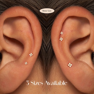 May include: Close-up of two ears, each with three small, gold-coloured flower-shaped earrings. Each earring has a central, clear gemstone surrounded by smaller, clear gemstones. The text "New Size" and "3 Sizes Available" are visible.