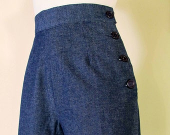 May include: Dark blue denim shorts with a high waist and button detailing on the side. The shorts have a cuffed hem.