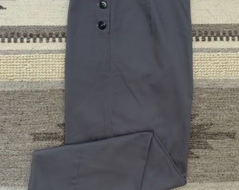 May include: Gray trousers with a high waist and a button closure. The pants have a wide leg and a folded hem. The trousers are made of a smooth fabric and are folded on a patterned rug.