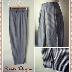 May include: Houndstooth-patterned trousers in black and white, hanging on a wooden hanger. The pants have a high waist, pleats, and a button closure. The image includes close-up shots of the fabric and details. The text "Swell Dame Athens" is visible.