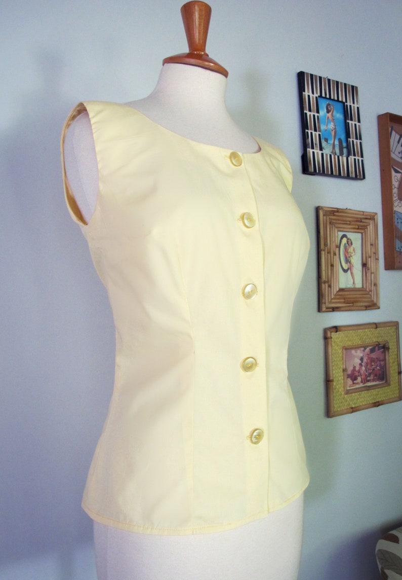 May include: A sleeveless, pale yellow blouse with a button-up front. The blouse has a fitted bodice and a slightly flared hem.