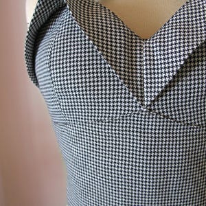 May include: A black and white houndstooth pattern top with a halter neckline. The top is fitted and has a structured design, showcasing a classic and timeless aesthetic. The fabric is a tightly woven material.