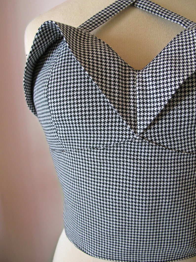 May include: A black and white houndstooth pattern top with a halter neckline. The top is fitted and has a structured design, showcasing a classic and timeless aesthetic. The fabric is a tightly woven material.