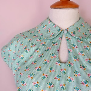 May include: A light blue dress with a white collar and a floral print. The dress has a keyhole opening at the neckline and short sleeves.