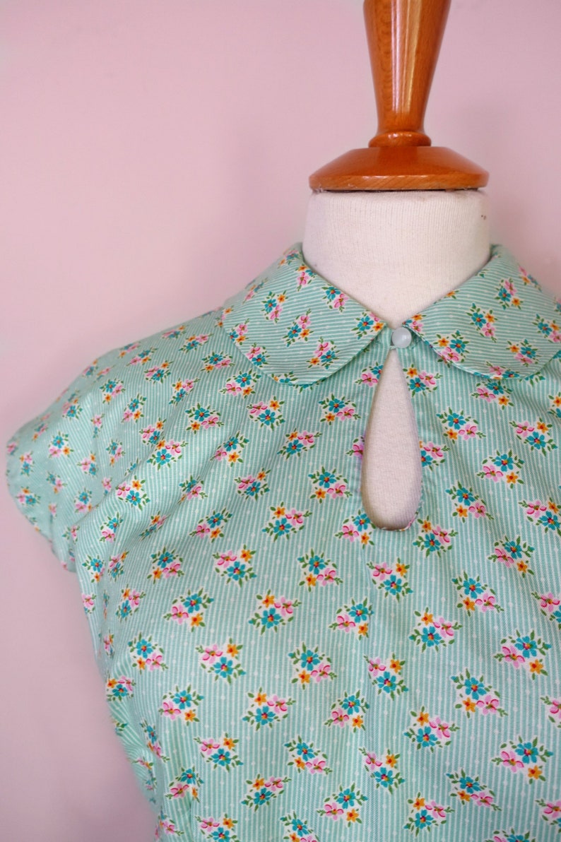May include: A light blue dress with a white collar and a floral print. The dress has a keyhole opening at the neckline and short sleeves.