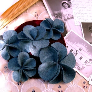 Puede incluir: Una pinza para el pelo de terciopelo burdeos con cinco adornos de flores de fieltro azul. Las flores est&aacute;n hechas de varias capas de fieltro, creando un efecto tridimensional.