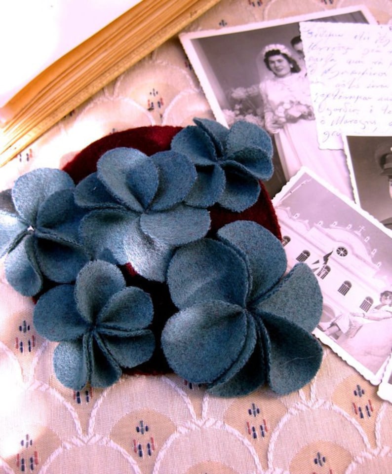 Puede incluir: Una pinza para el pelo de terciopelo burdeos con cinco adornos de flores de fieltro azul. Las flores est&aacute;n hechas de varias capas de fieltro, creando un efecto tridimensional.