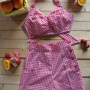 May include: Red and white gingham halter top and matching shorts. The top has a sweetheart neckline and a tie closure at the back. The shorts have a high waist and button closures on the side.