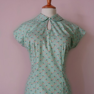 May include: A mint green blouse with a white collar and a floral print. The blouse has a keyhole opening at the neckline and short sleeves.