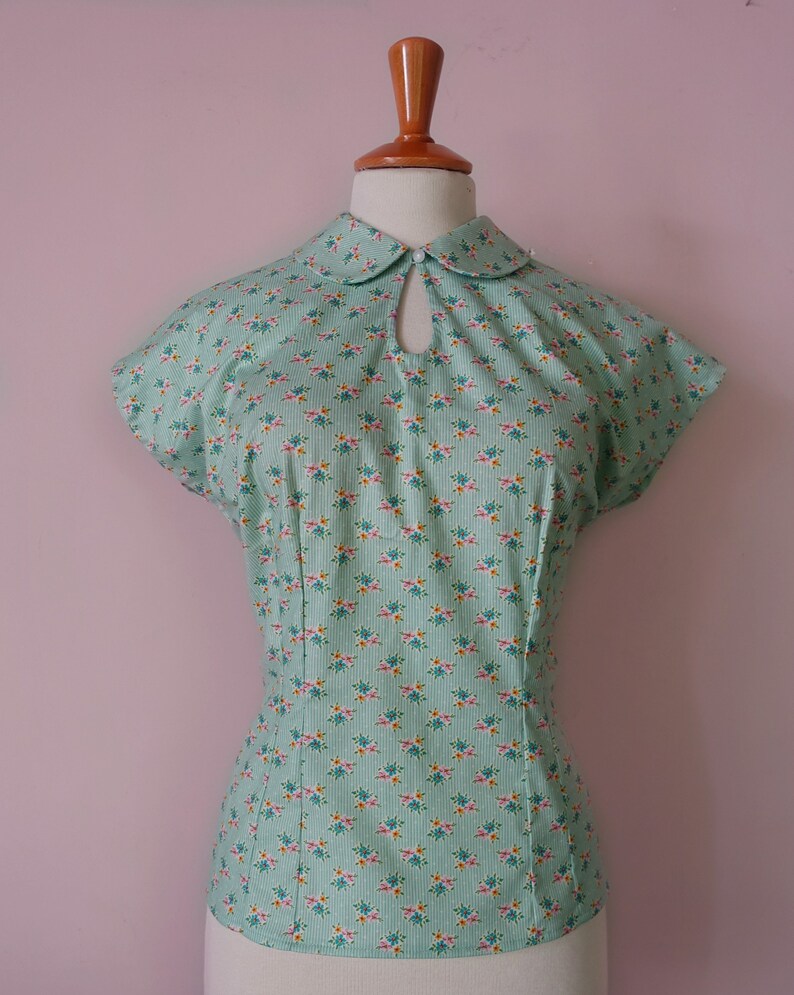 May include: A mint green blouse with a white collar and a floral print. The blouse has a keyhole opening at the neckline and short sleeves.